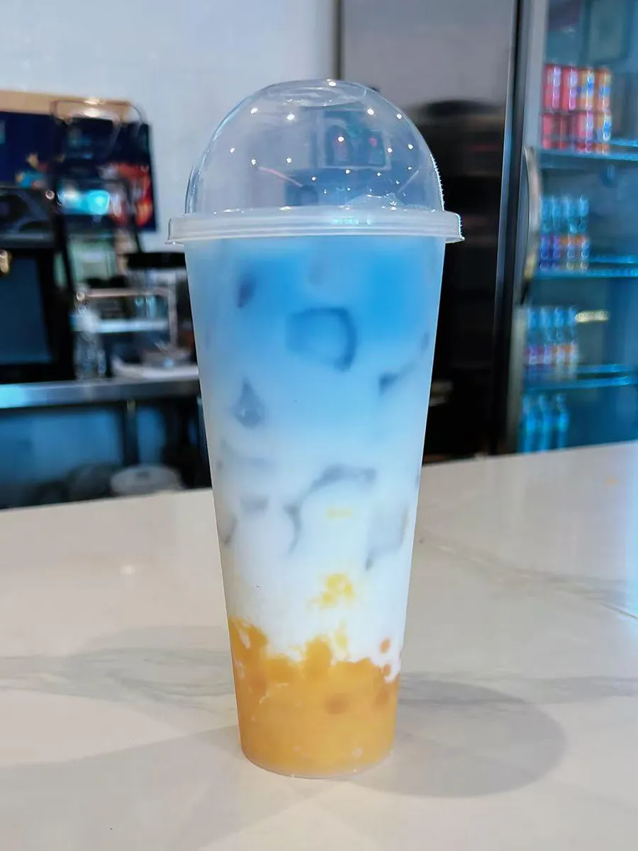 Blue butterfly pea mango layered milk tea ice cubes tall dome plastic cup shop interior at Mochi & Crunch Treats, a Modern Dessert Café in Tupelo