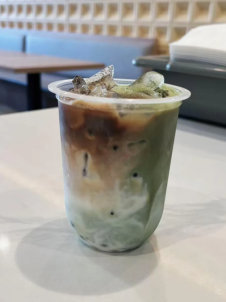 Layered matcha coffee milk iced bubble tea transparent cup marble counter at Mochi & Crunch Treats, a Modern Dessert Café in Tupelo